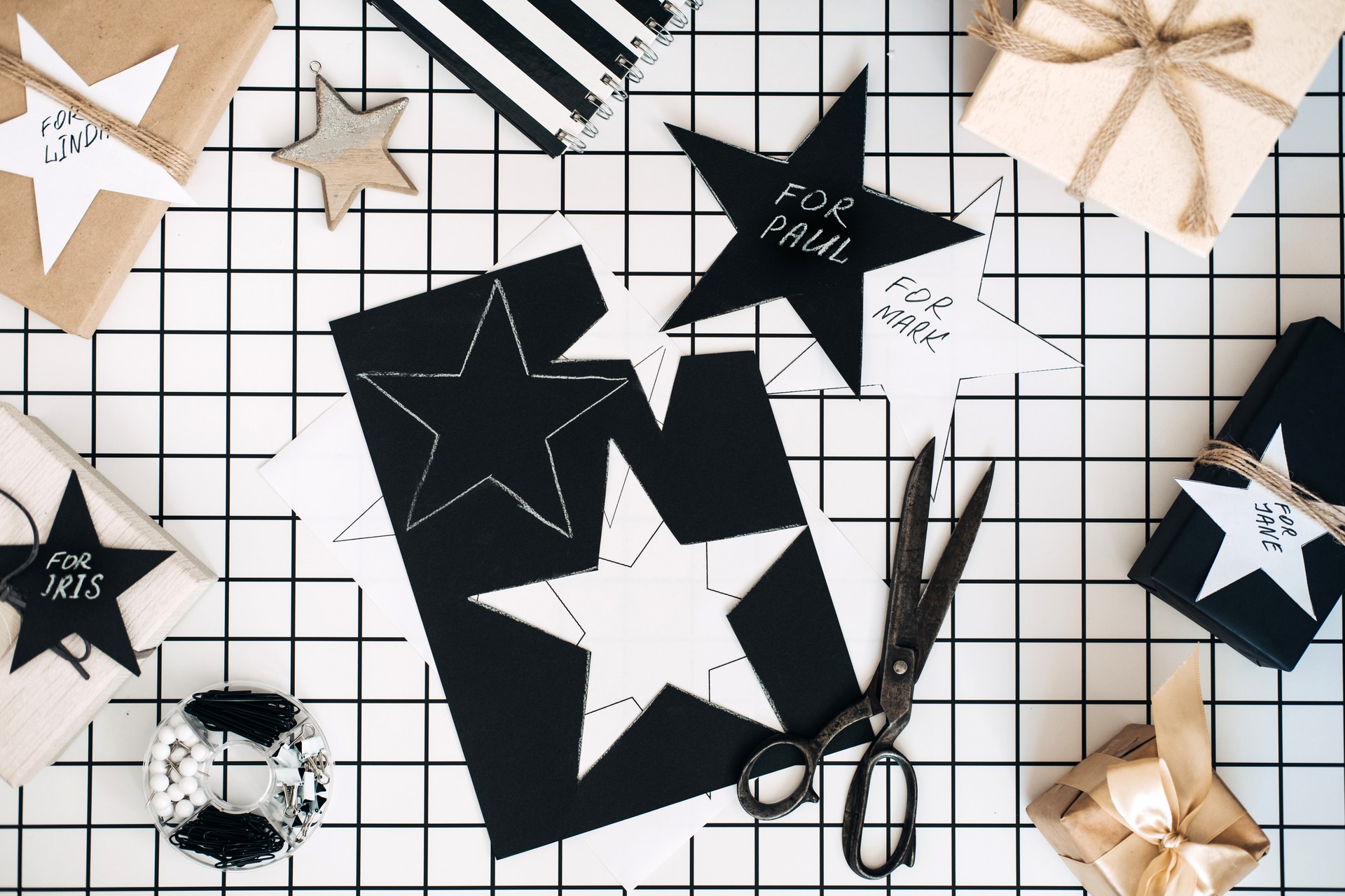 Personalized gifts. Modern black and white flat lay with Christmas gift wrapping process. Scissors, wrapped craft boxes signed names and wrapping tools on white checkered background